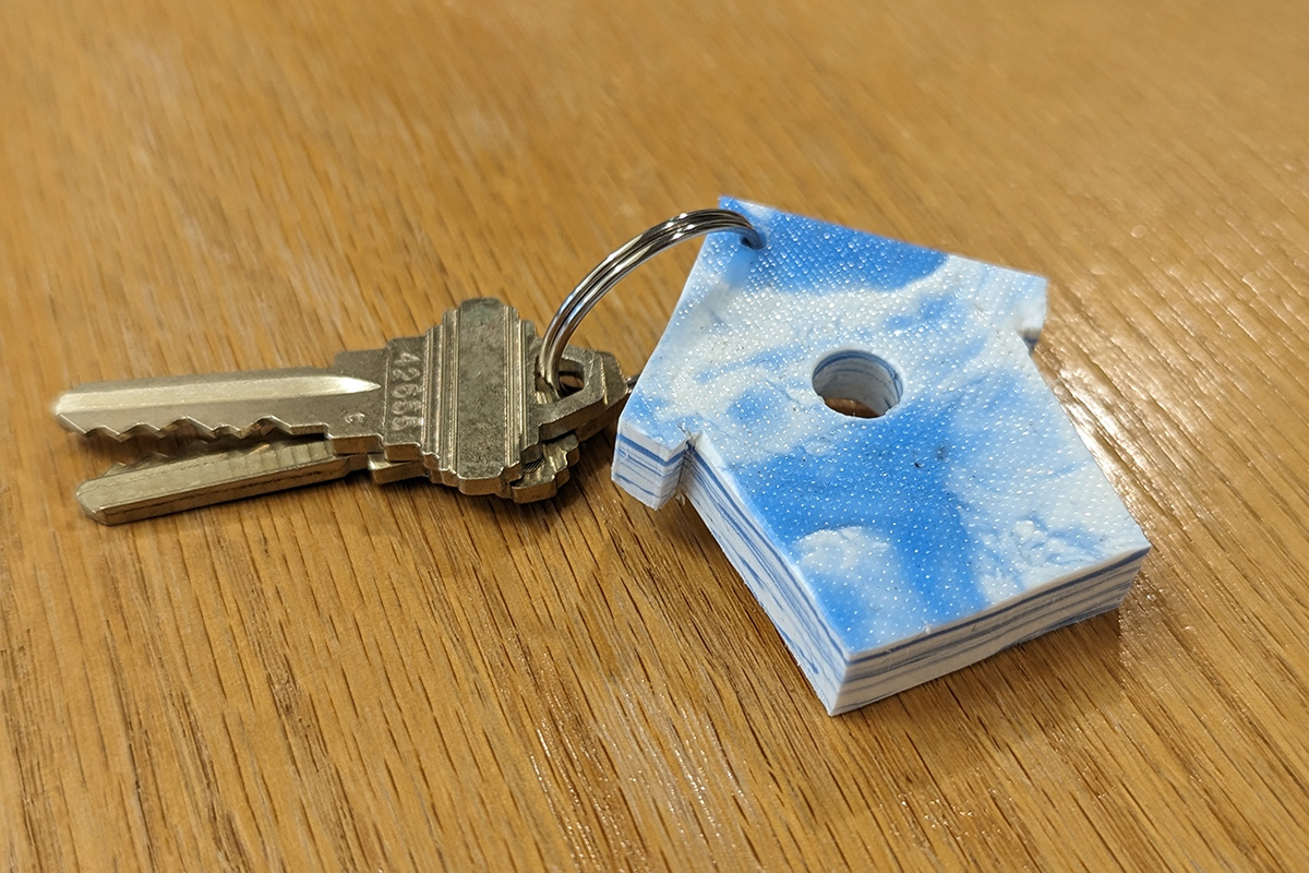 A keychain in birdhouse shape made from 100% recycled post-consumer products. Blue from detergent bottles and white from milk jugs.