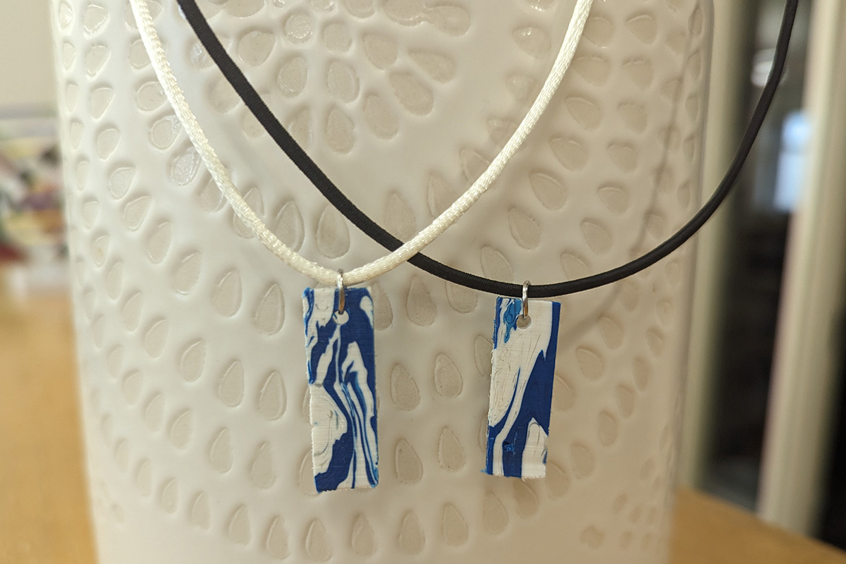 A necklace pendant made from 100% recycled post-consumer products. Blue from detergent bottles and white from milk jugs.